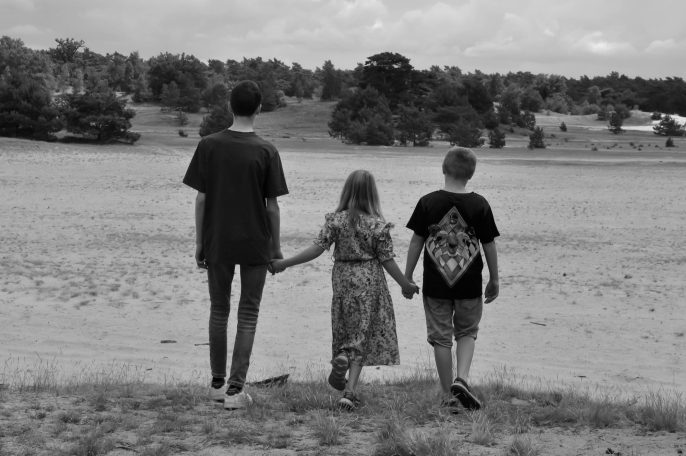 Drie kinderen staan hand in hand in een uitgestrekt, open landschap.