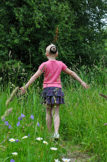 Meisje met een korte rok wandelt door een weelderig groen grasveld met bloemen.