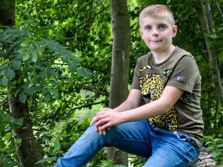 portret van Marijn Jongen met kort blond haar zit op een boomstronk in een groene omgeving.