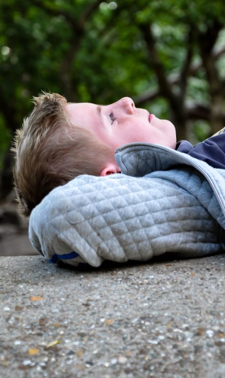 Jongeman met een kussen, liggend op een stenen vloer, omringd door groen.