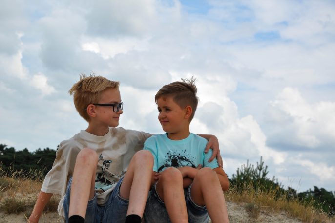 Twee jongens zitten samen op een heuvel en kijken elkaar vriendelijk aan.