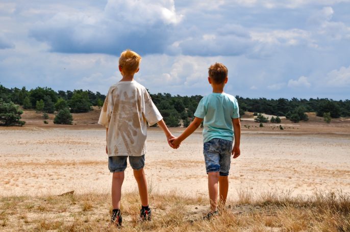 Twee kinderen staan hand in hand, kijkend naar een dorre, droge landschap.