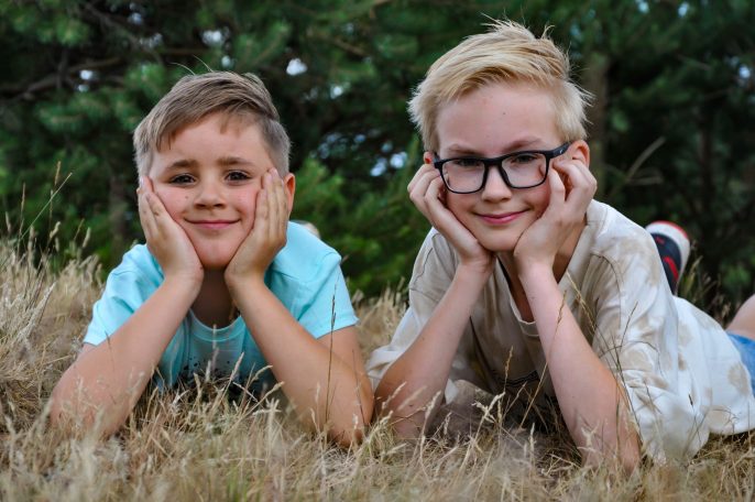 Twee kinderen liggen in het gras, met hun handen onder hun kin en glimlachend.
