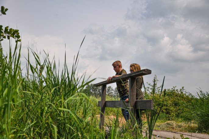 Twee mensen staan op een brug en kijken naar de omgeving, omringd door groen.