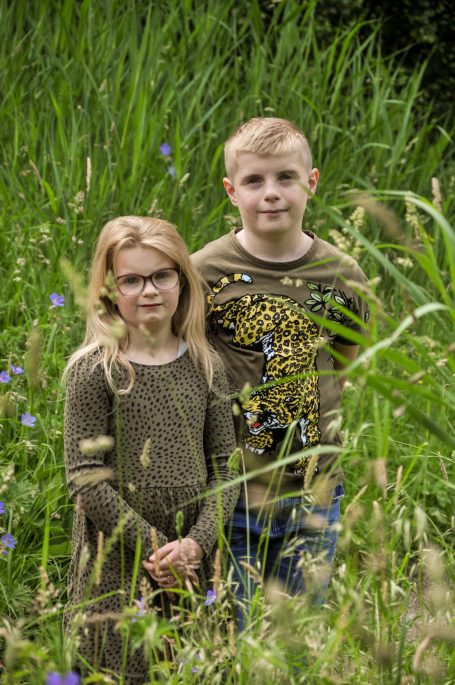 Twee kinderen staan in een groene omgeving met wilde bloemen.